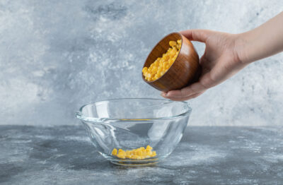 female hand starting add sweet corns into glass bowl scaled