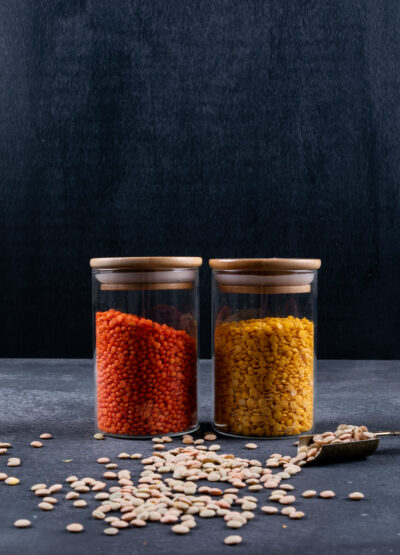 side view red yellow lentils glassy jar with iron spice spoon dark stone black table scaled